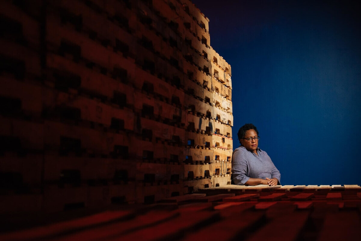 A portrait of Artist Juana Valdes framed by a wall of shipping pallets in her installation. Image courtesy of photographer Pedro Wazzan and Locust Projects.