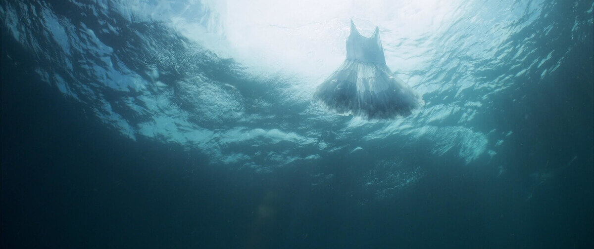 Image depicting a translucent dress floating beneath the ocean’s meniscus. Video still courtesy of Juana Valdes.